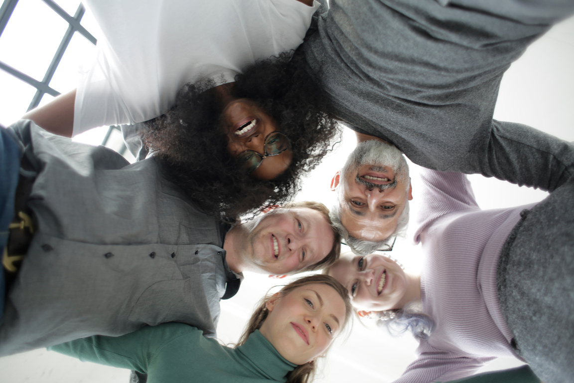 From below of cheerful multiethnic coworkers embracing each other in circle during team building in office